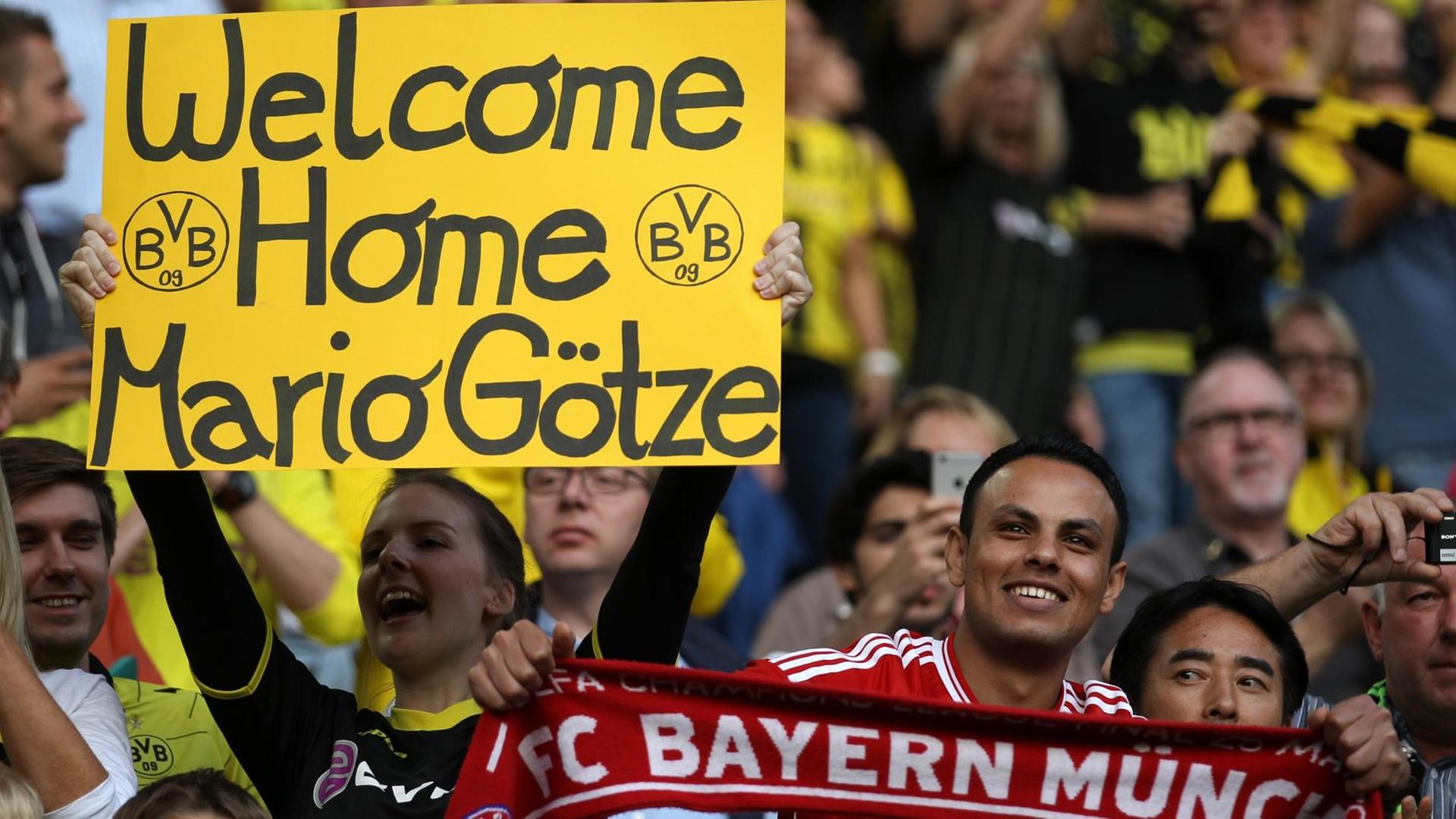 Ein Fan von Dortmund hält ein Schild mit der Aufschrift "Welcome Home Mario Götze" hoch. Rechts ein Fan von Bayern München.