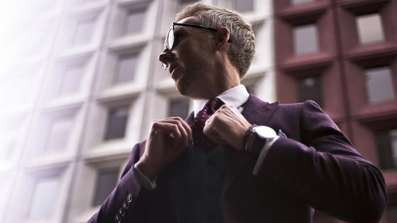 Fashion-Blogger Steve Tilbrook, im Anzug mit Armbanduhr, rückt sich seine Krawatte zurecht.