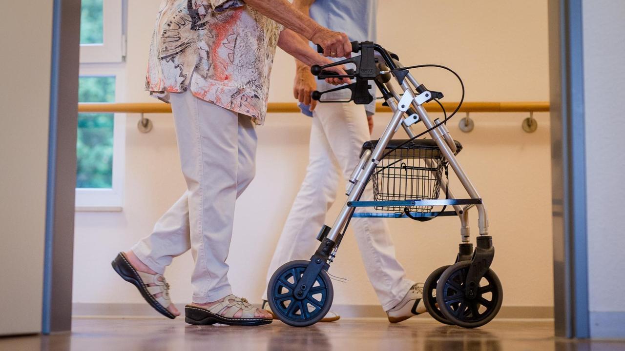 Eine Pflegekraft geht in einem Pflegeheim mit einer älteren Frau über einen Korridor.