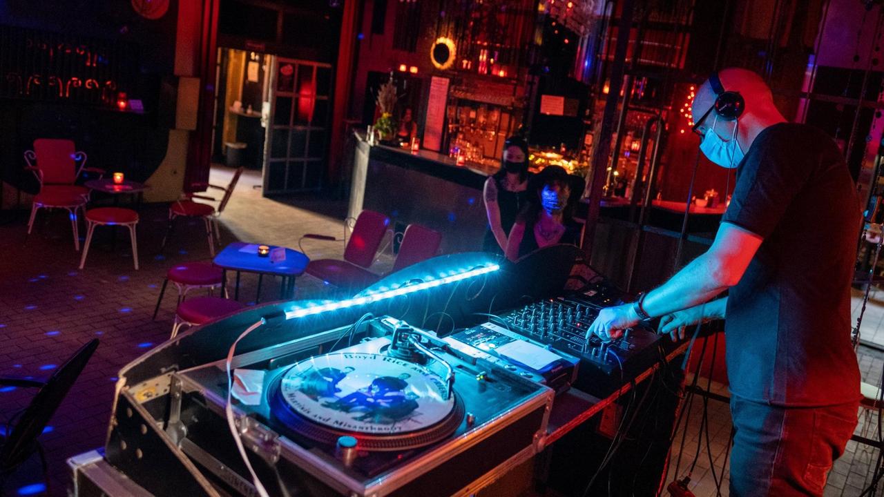 Ein DJ arbeitet mit Mundschutz am Mischpult in einem leeren Musikclub Ein DJ arbeitet mit Mundschutz am Mischpult in einem leeren Musikclub
