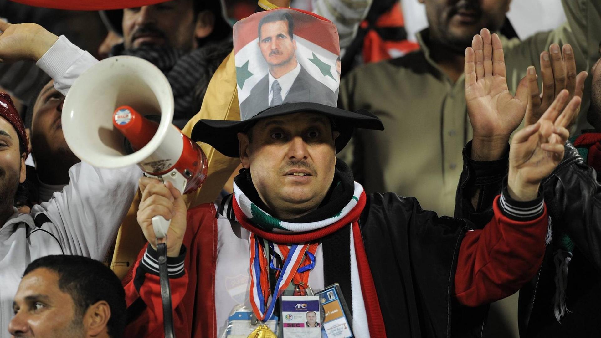 Ein syrischer Fußballfan mit Megaphon trägt bei einem Spiel des Asiencups 2011 das Konterfei von Präsident Baschar al Assad auf dem Hut.
