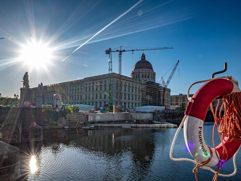Blick auf das Humboldt Forum Berlin am Schlossplatz gegen die Sonne, im Vordergrund ein Rettungsreifen und die Spree