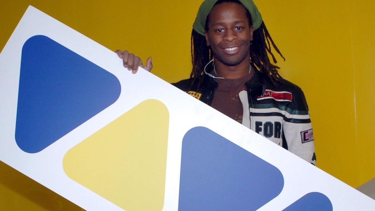 Der VIVA-Moderator Mola Adebisi hält ein Schild mit dem Logo des Musiksenders in Händen.