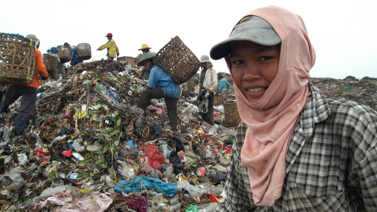 Straßenkinder sammeln Müll auf einer Müllhalde in Malaysia. Im Vordergrund lächelt ein junges Mädchen mit Kopftuch und Baseballkap, 2013
