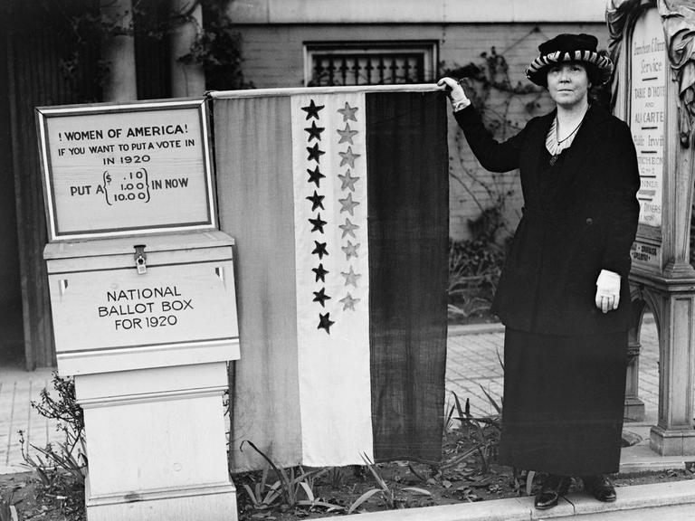 Suffragetten Protest in den USA (04.02.1916). Eine Frau sammelt Geld für die Frauenwahlrechtsbewegung. Sie steht vor eine Kiste mit der Aufschrift: "Women of America! If you want to put a vote in in 1920 put a (.10, 1.00, 10.00) in Now, National Ballot Bo