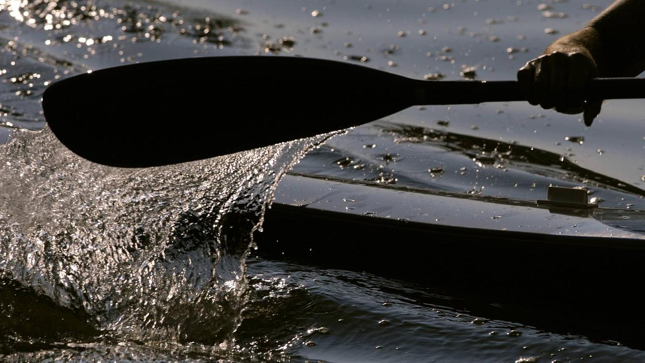 Der deutsche Kajak-Vierer der Männer verpasste eine Medaille. Es ist ein Stück von einem Kajak zu sehen und eine Hand, die ein Paddel durch das Wasser zieht. Der deutsche Kajak-Vierer der Männer verpasste eine Medaille. Es ist ein Stück von einem Kajak zu sehen und eine Hand, die ein Paddel durch das Wasser zieht.