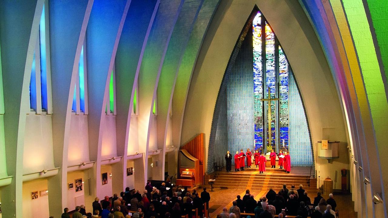 Ein einer bunt beleuchteten Kirche steht das Ensemble im Halbkreis im Altarraum.