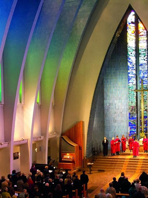 Ein einer bunt beleuchteten Kirche steht das Ensemble im Halbkreis im Altarraum.