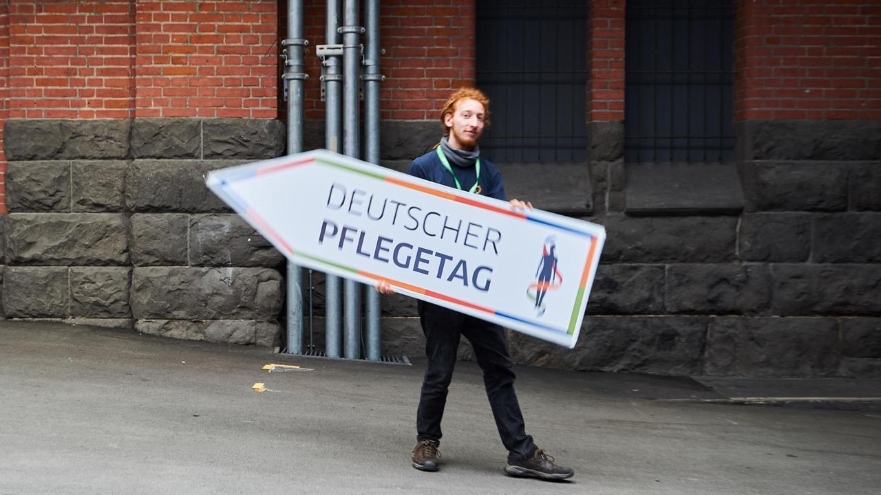 Ein Mann hält in Berlin ein Schild mit der Aufschrift "Deutscher Pflegetag" in den Händen.