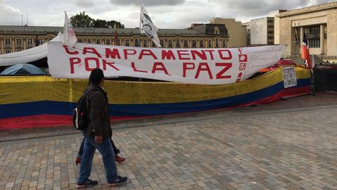 Ein Transparent hängt vor einem Zeltcamp, Aufschrift: "Campamento por la Paz" - deutsch: Lager für den Frieden