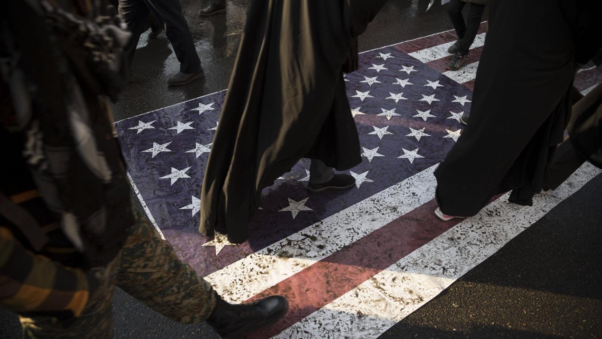 Menschen laufen während einer Trauerfeier in der iranischen Hauptstadt Teheran über eine amerikanische Flagge