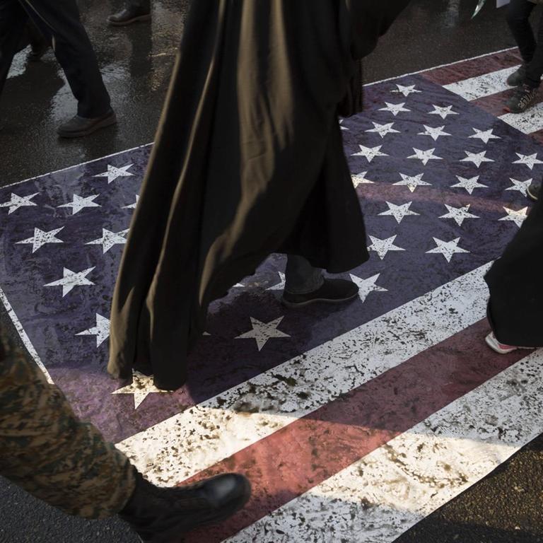 Menschen laufen während einer Trauerfeier in der iranischen Hauptstadt Teheran über eine amerikanische Flagge