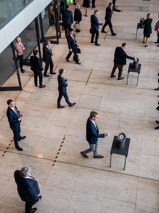 Das Foto zeigt eine Stimmenabgabe im Bundestag mit mehreren aufgestellten Wahlurnen. Auf dem Boden davor befinden sich Striche, damit die Abgeordneten wegen Corona einen Sicherheitsabstand einhalten.