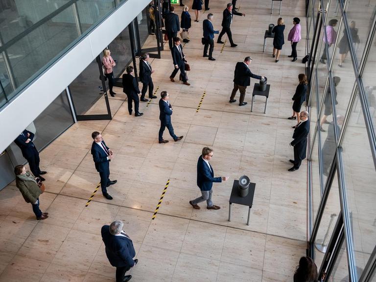 Das Foto zeigt eine Stimmenabgabe im Bundestag mit mehreren aufgestellten Wahlurnen. Auf dem Boden davor befinden sich Striche, damit die Abgeordneten wegen Corona einen Sicherheitsabstand einhalten.