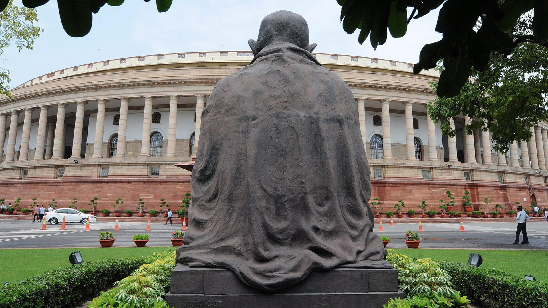 Das indische Parlament in Neu Dehli, im Vordergrund eine Statue von Mahatma Gandhi