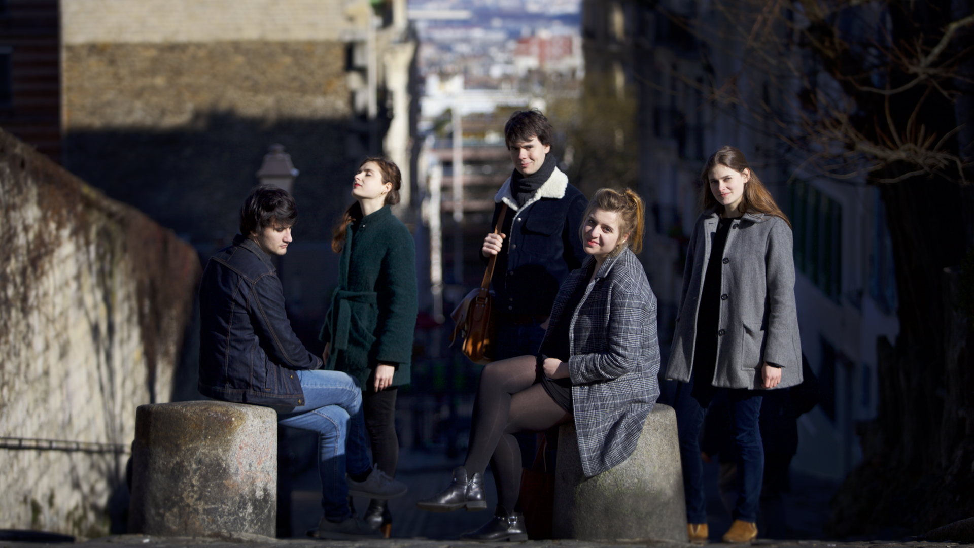 Das französische Ensemble Le Consort besteht aus fünf Migliedern, zwei Männern, drei Frauen, die sich in Winterkleidung zum Teil sitzend, zum Teil stehend in einer Gasse positioniert haben.