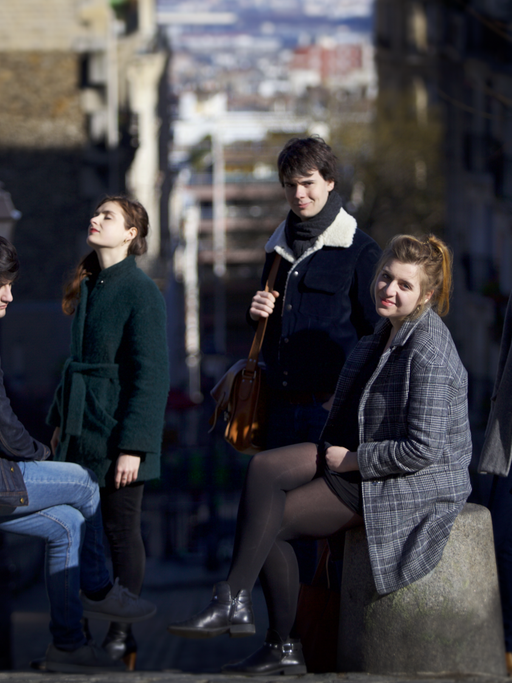 Das französische Ensemble Le Consort besteht aus fünf Migliedern, zwei Männern, drei Frauen, die sich in Winterkleidung zum Teil sitzend, zum Teil stehend in einer Gasse positioniert haben.