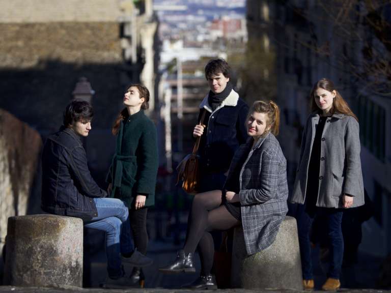 Das französische Ensemble Le Consort besteht aus fünf Migliedern, zwei Männern, drei Frauen, die sich in Winterkleidung zum Teil sitzend, zum Teil stehend in einer Gasse positioniert haben.