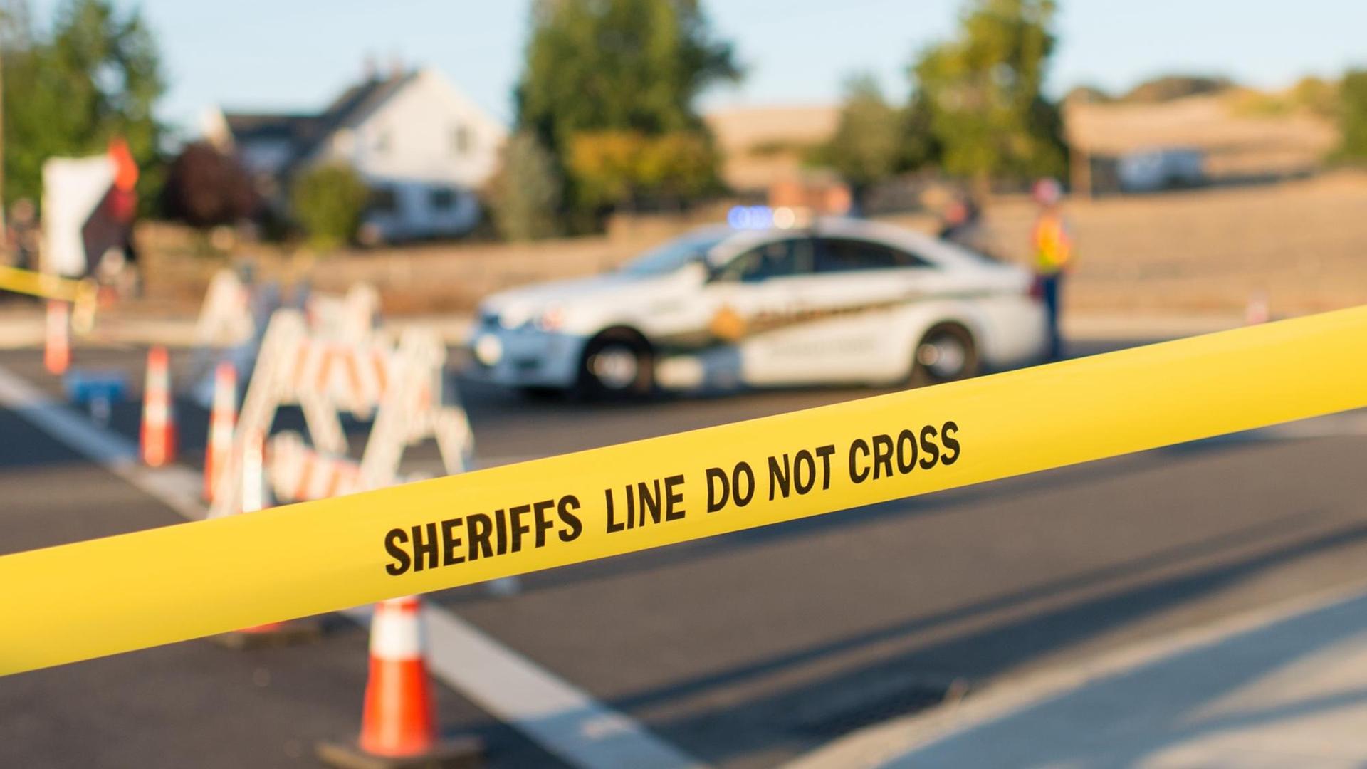 Hinter der Absperrung mit der Aufschrift "Sheriffs Line do not cross" ist ein Polizeiauto zu sehen.