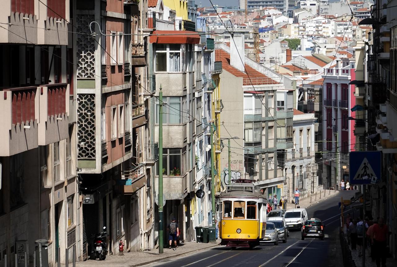 Eine Straßenbahn der Linie 28 fährt einen Berg hoch durch ein Wohnviertel von Lissabon.