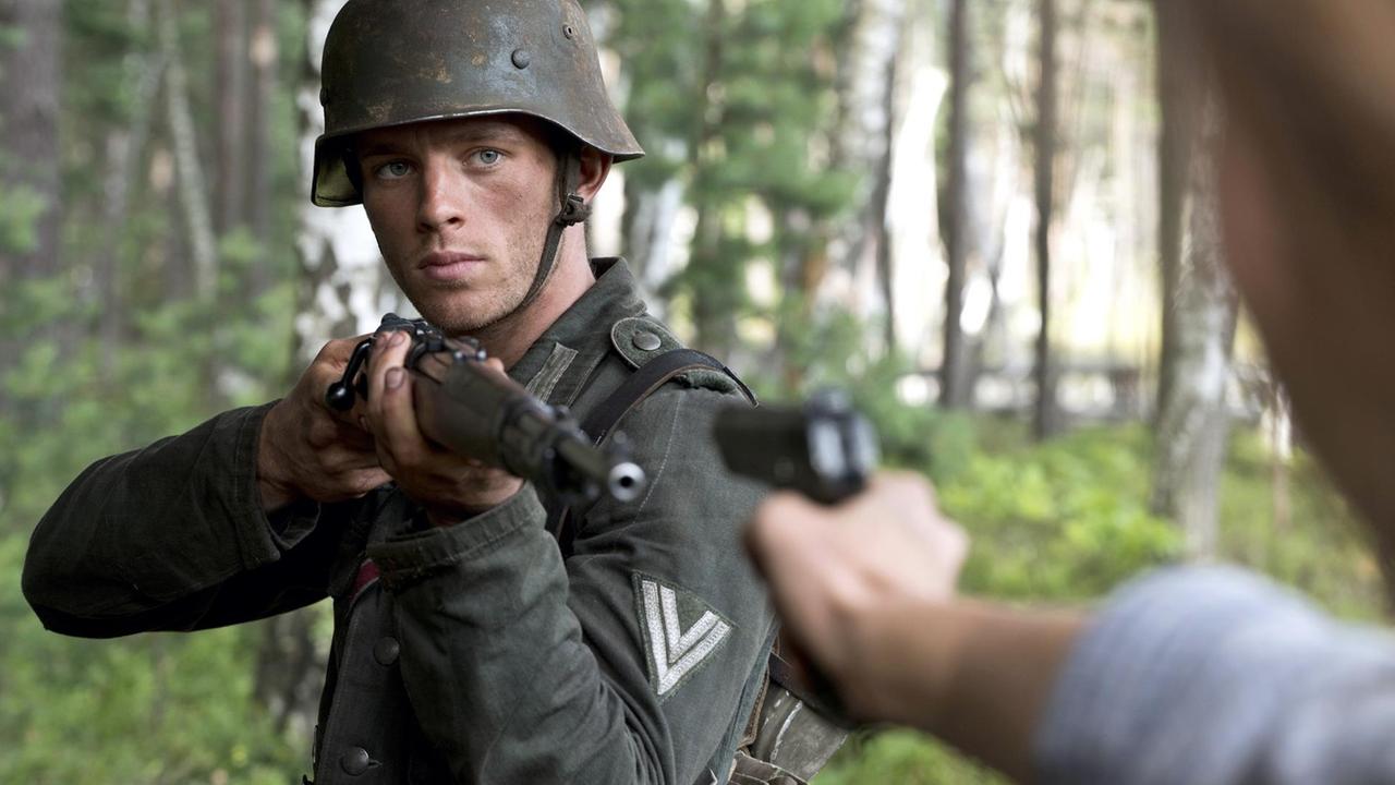 Ein Wehrmachtssoldat richtet das Gewehr auf eine Person, die ihn mit einer Pistole bedroht.