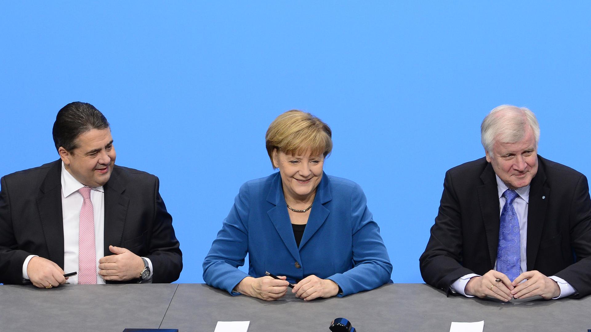 Der SPD-Vorsitzende Sigmar Gabriel, Bundeskanzlerin Angela Merkel (CDU) und CSU-Chef Horst Seehofer sitzen an einem Tisch und unterzeichnen den Koalitionsvertrag.