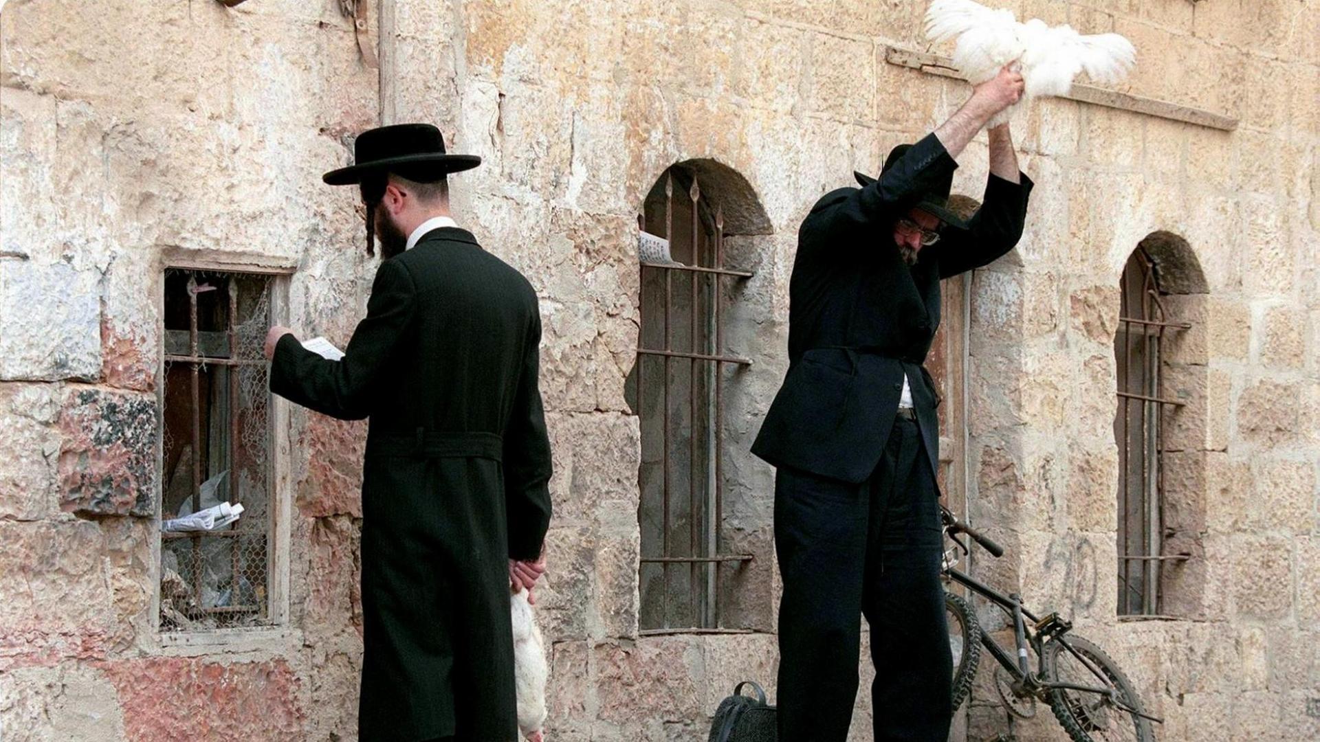 Zwei orthodoxe Juden im Jerusalemer Viertel Mea Shearim: Einer betet gegen eine Mauer, der andere schwingt ein Huhn über seinem Kopf