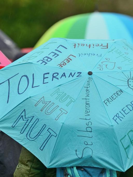 Auf einem blauen Regenschirm sind u.a. die Worte Frieden, Mut, Toleranz und Liebe zu lesen.