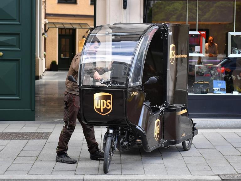 Ein Paketzusteller der Firma UPS steht auf der Straße neben seinem Lastenrad.