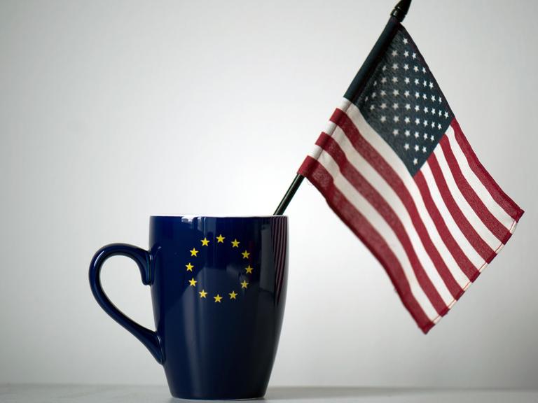 In einer Tasse mit einem EU-Symbol steckt eine US-Fahne.