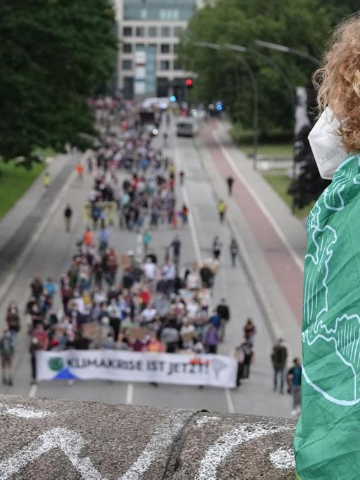 Ein Mensch mit einer Fahne mit dem Logo von Fridays for Future verfolgt von einer Brücke aus die Demonstration des Bündnisses Fridays for Future entlang einer Straße.