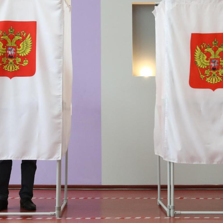 Das Bild zeigt zwei Wahlkabinen während der Parlamentswahl in Russland. In der linken steht ein Mann, es sind seine Beine unter dem Vorhang zu sehen.