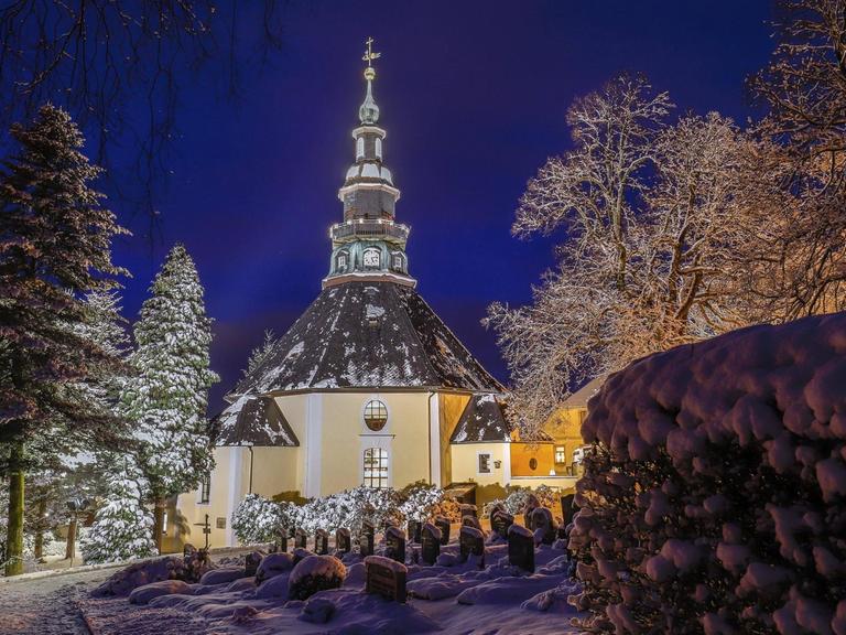 Festlich beleuchtet in der Blauen Stunde ist die Bergkirche im verschneiten weihnachtlichen Seiffen. Viele Touristen besuchen in der Weihnachtszeit den Ort im Erzgebirge mit seinen vielen Herstellern von traditioneller Erzgebirgsicher Volkskunst.