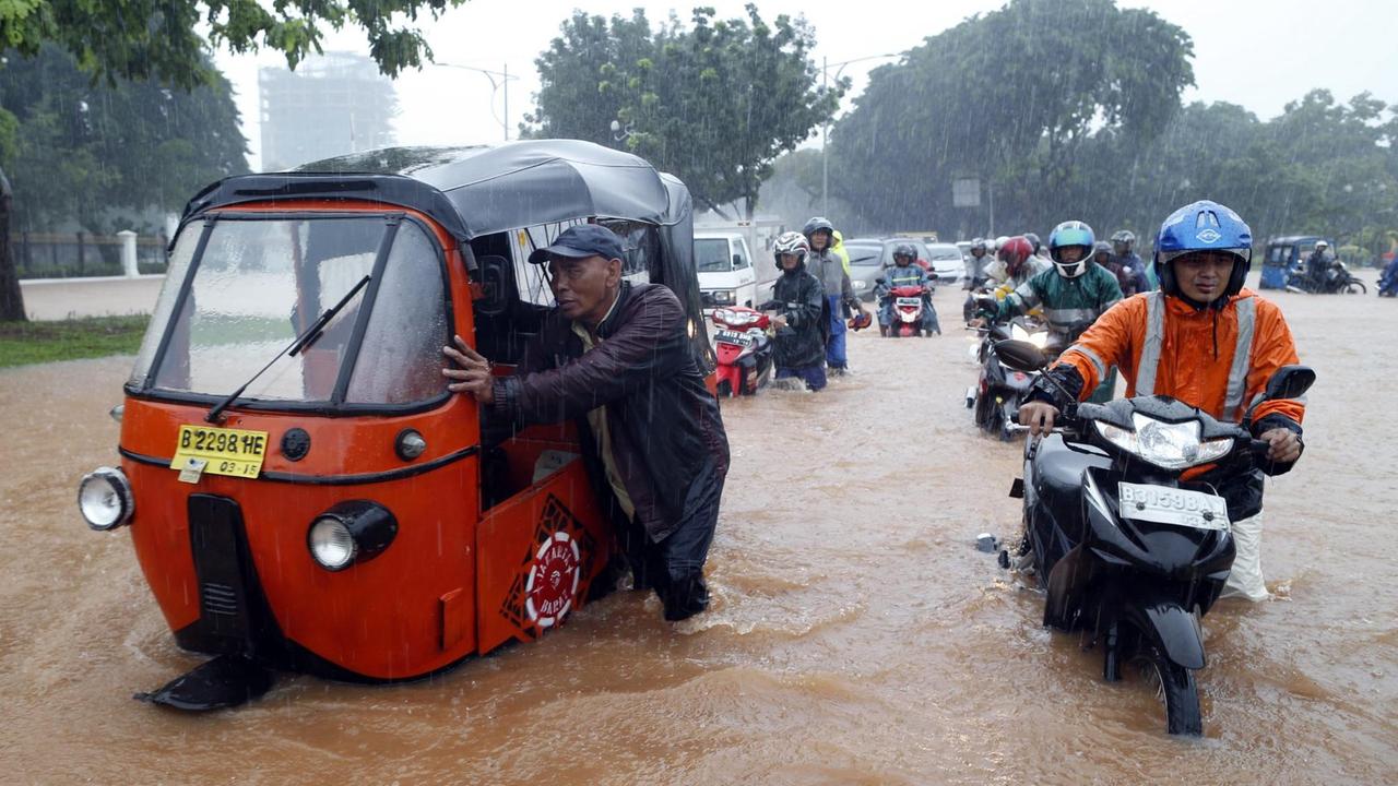 Ein Motorradfahrer fährt durch überschwemmte Straßen Jakartas