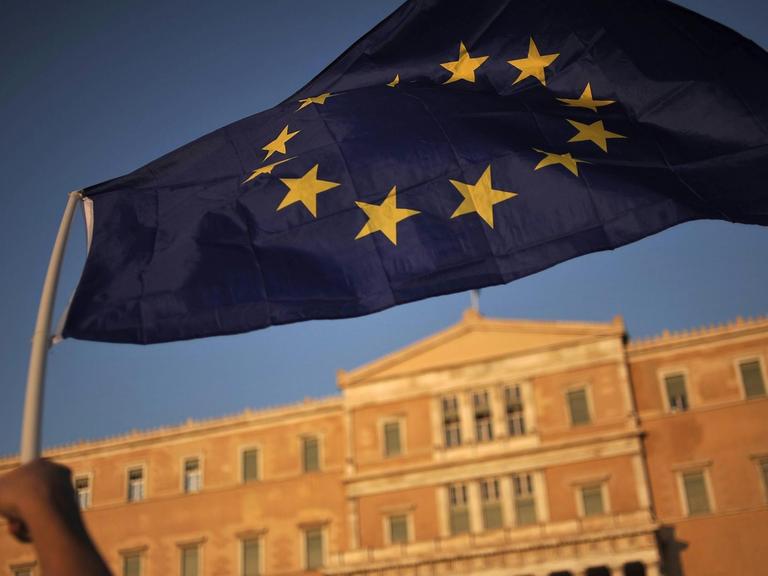 Eine Hand schwenkt eine EU-Fahne vor dem griechischen Parlament in Athen.