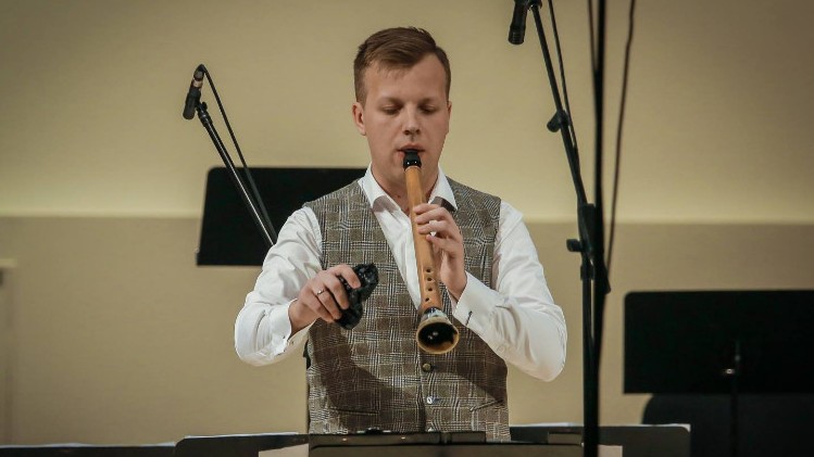 Ein Mann spielt ein flötenartigen Instrument aus Holz und Horn hinter einem Notenständer.