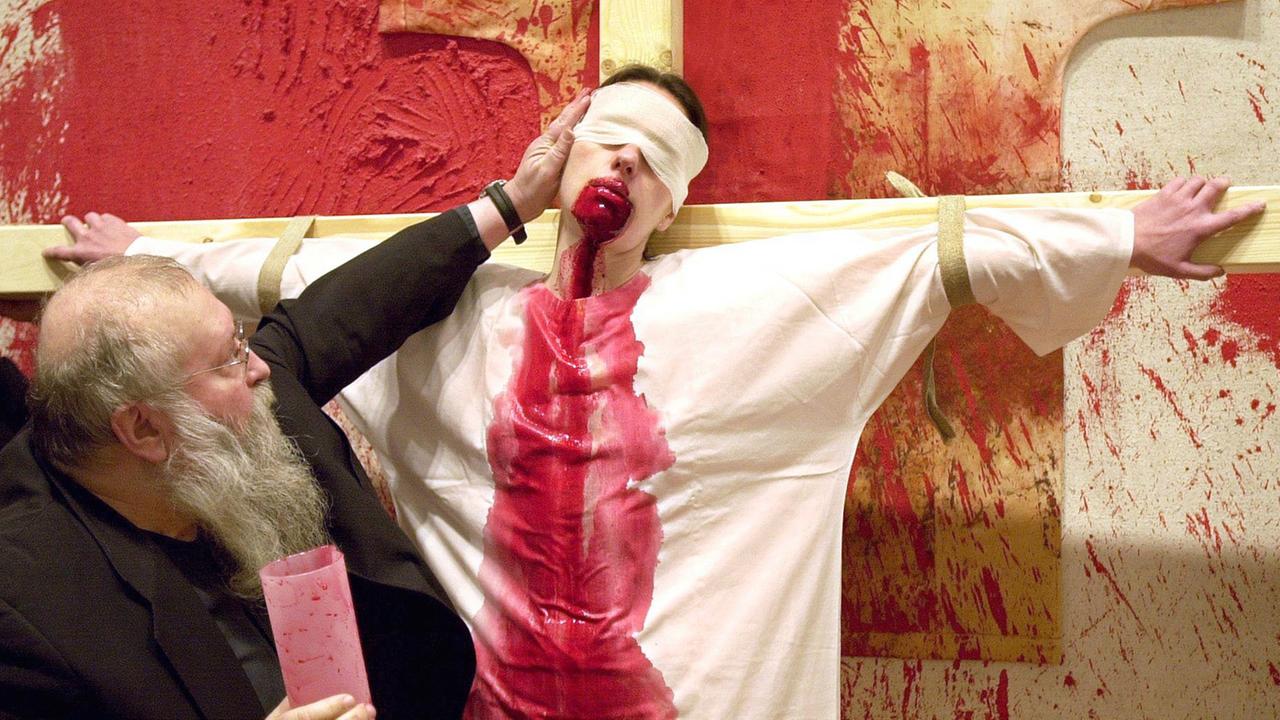 Der österreichische Künstler Hermann Nitsch rückt während einer Blut-Performance im Dezember 2001 im Frankfurter Museum Schirn den Kopf eines an ein Kreuz gebundenen Models zurecht. Aus dem Mund der Frau rinnt Schweineblut, welches ihr Nitsch zuvor eingeflößt hatte. In wechselnder Reihenfolge goss der 63-Jährige Blut, Eigelb, Wasser und weißen Kleister in ihren Mund. Dann ließ sie die Flüssigkeiten auf ihr weißes Gewand rinnen.