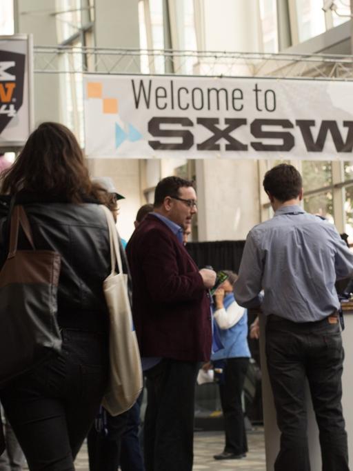 Menschen stehen vor einem Stand auf der Konferenz South by Southwest in Austin. Darüber hängt ein Transparent mit der Aufschrift SXSW.