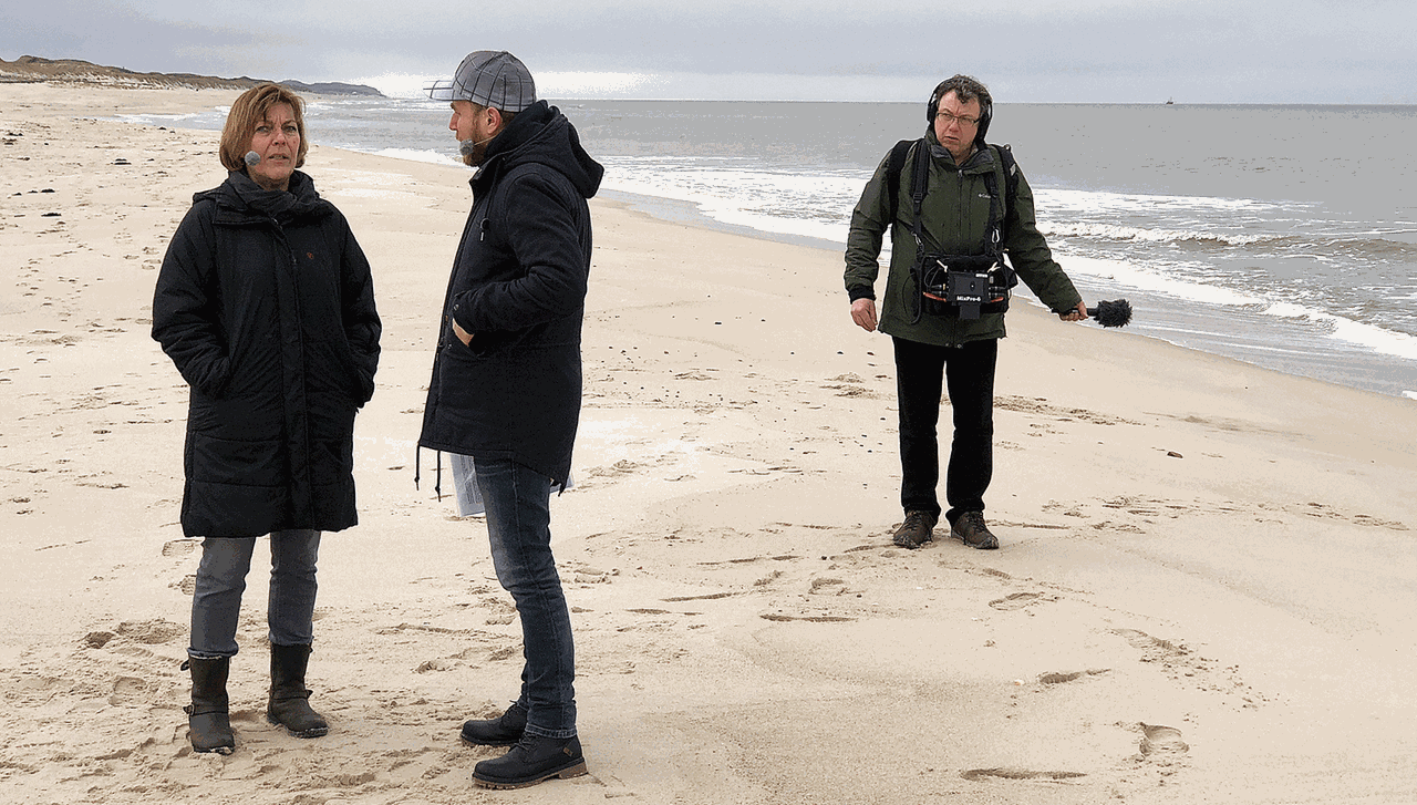 Dora Held im Gespräch mit Olaf Kosert am Strand von Sylt. Techniker Thomas Schütt nimmt das Geräusch der Wellen auf.