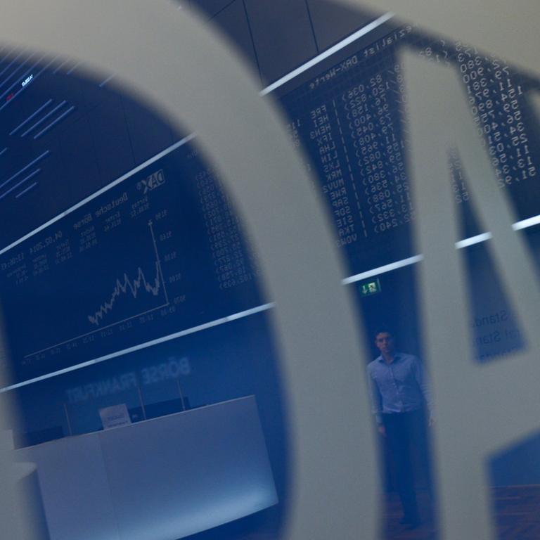 In einem Schild mit dem Dax-Logo spiegelt sich der Frankfurter Börsensaal mit der Kursanziege