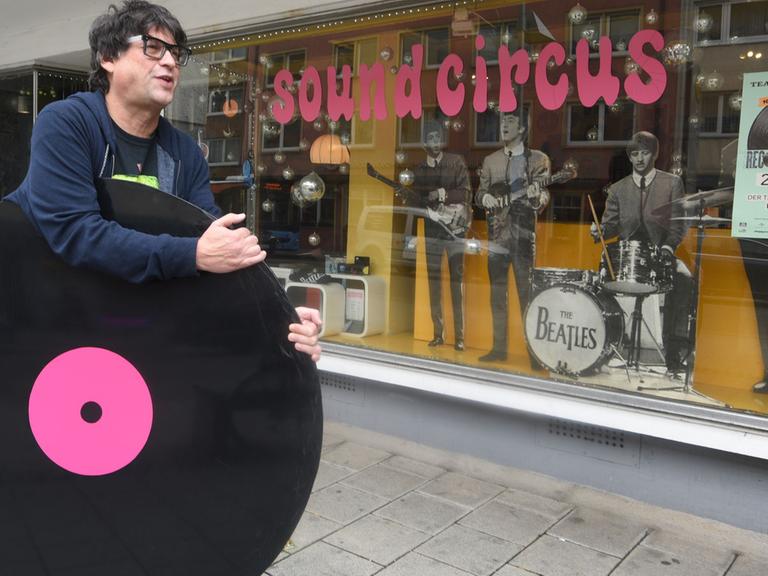 Martin Maag trägt in Ulm vor seinem Laden "Sound Circus" eine überdimensionale Schallplatte.
