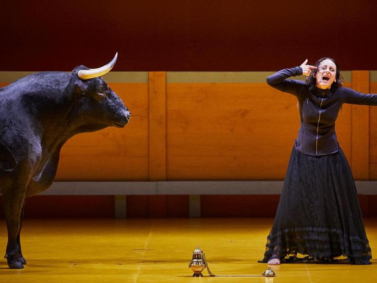 Szenenbild aus der Inzenierung "Liebestod" der katalanischen Regisseurin Angélica Liddell. Eine schreiende Frau im schwarzen Kleid steht neben einem Stier.