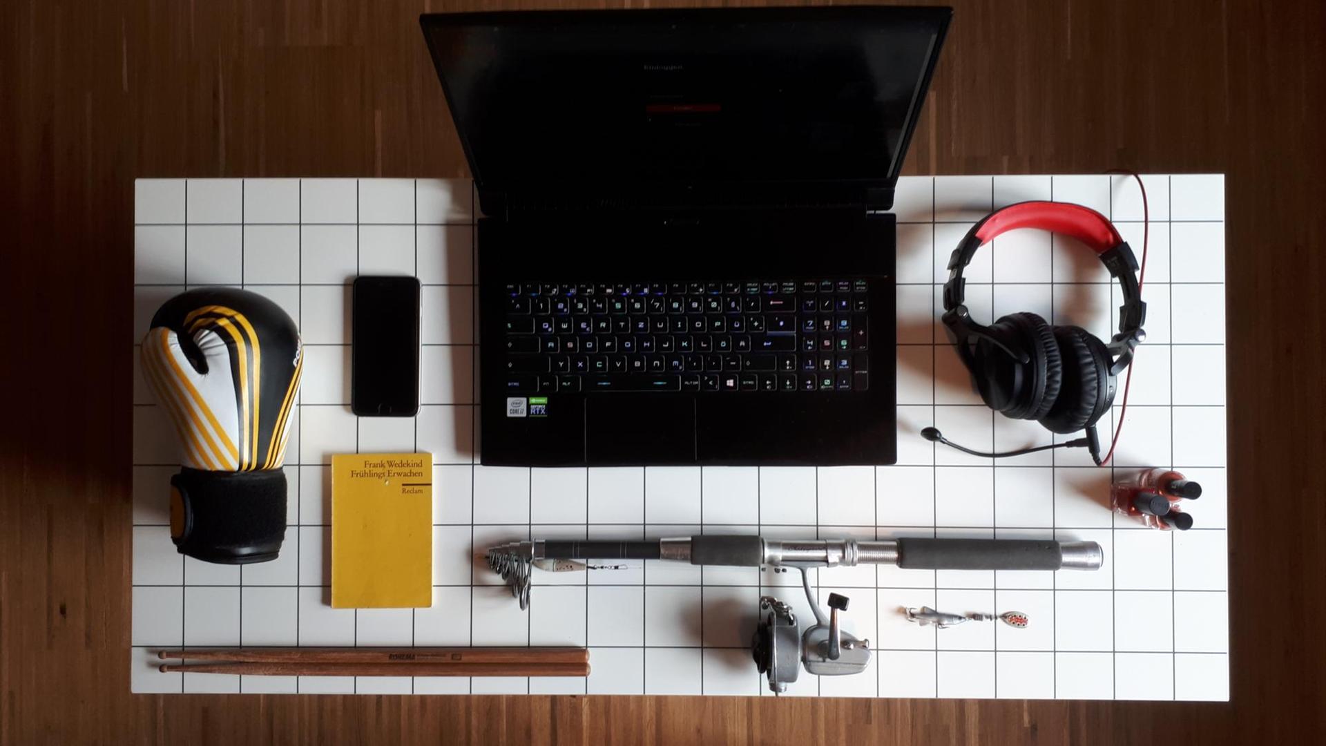 Schreibtisch mit Rechner, Reclamheft, Angel, Headset, Handy, Nagellack, Boxhandschuh, Drumsticks.