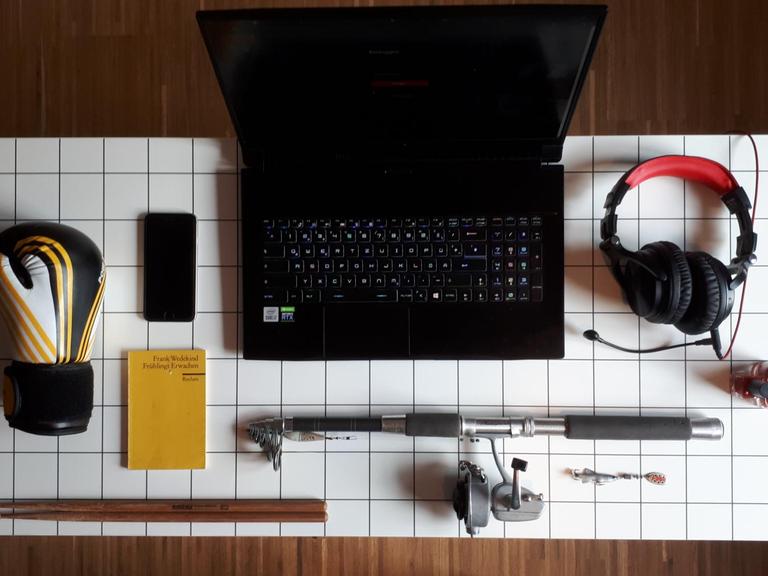Schreibtisch mit Rechner, Reclamheft, Angel, Headset, Handy, Nagellack, Boxhandschuh, Drumsticks.