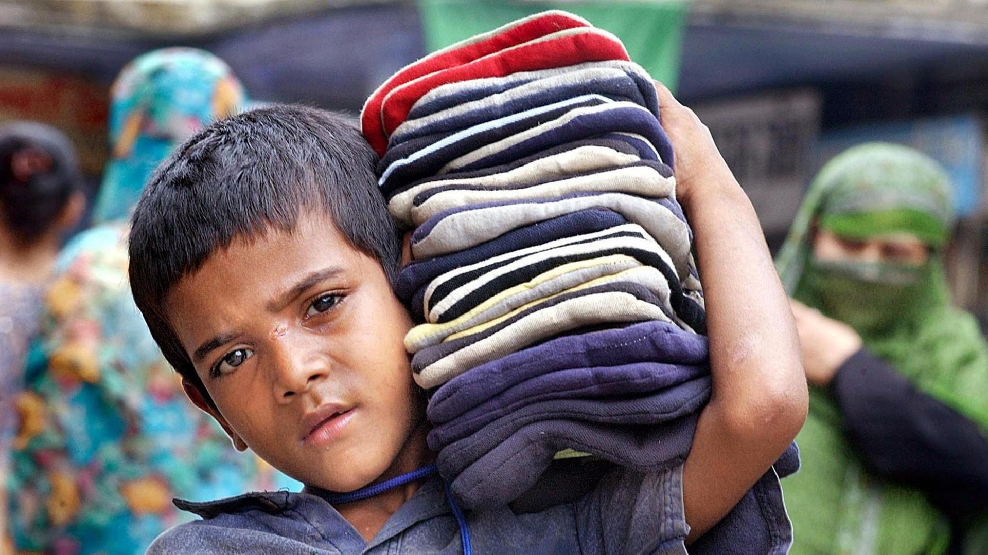 Viele Kinder in Indien müssen arbeiten, meist in Textilfabriken. Man sieht einen Jungen, der Stoffe auf der Schulter trägt.