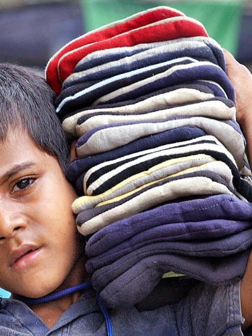 Viele Kinder in Indien müssen arbeiten, meist in Textilfabriken. Man sieht einen Jungen, der Stoffe auf der Schulter trägt.