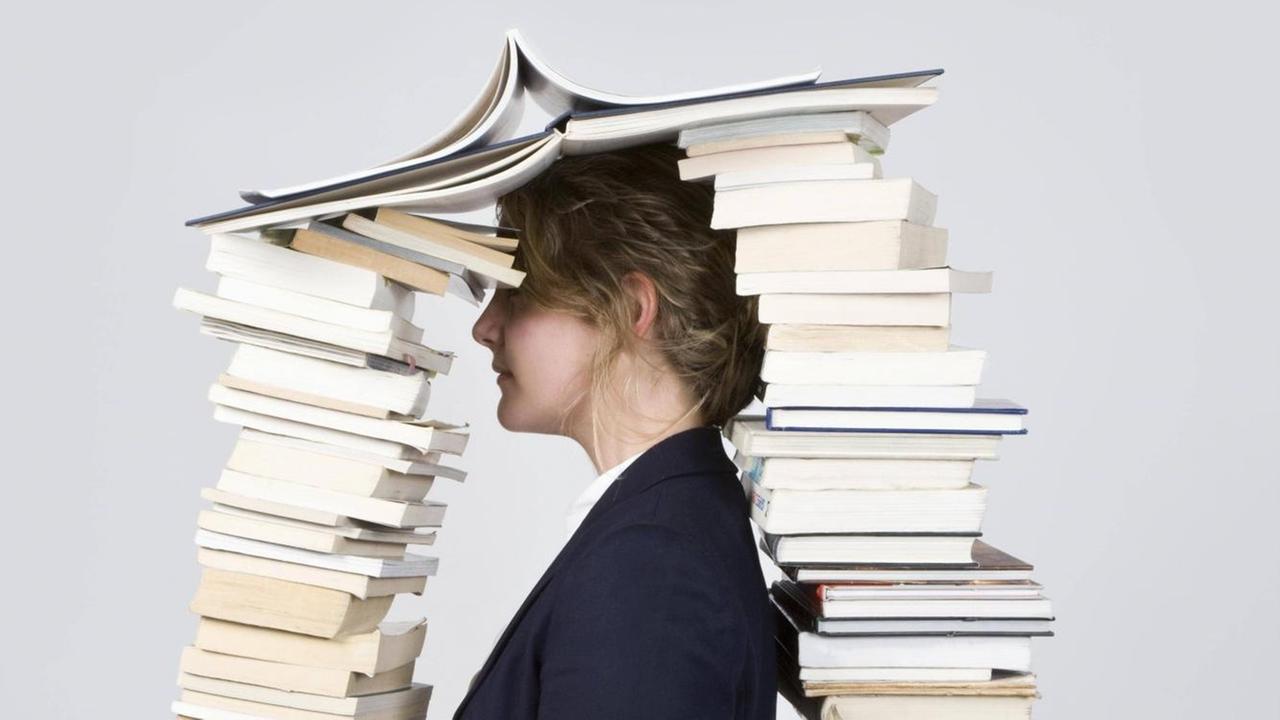 Eine Frau mit dem Kopf zwischen zwei hohen Bücherstapeln.