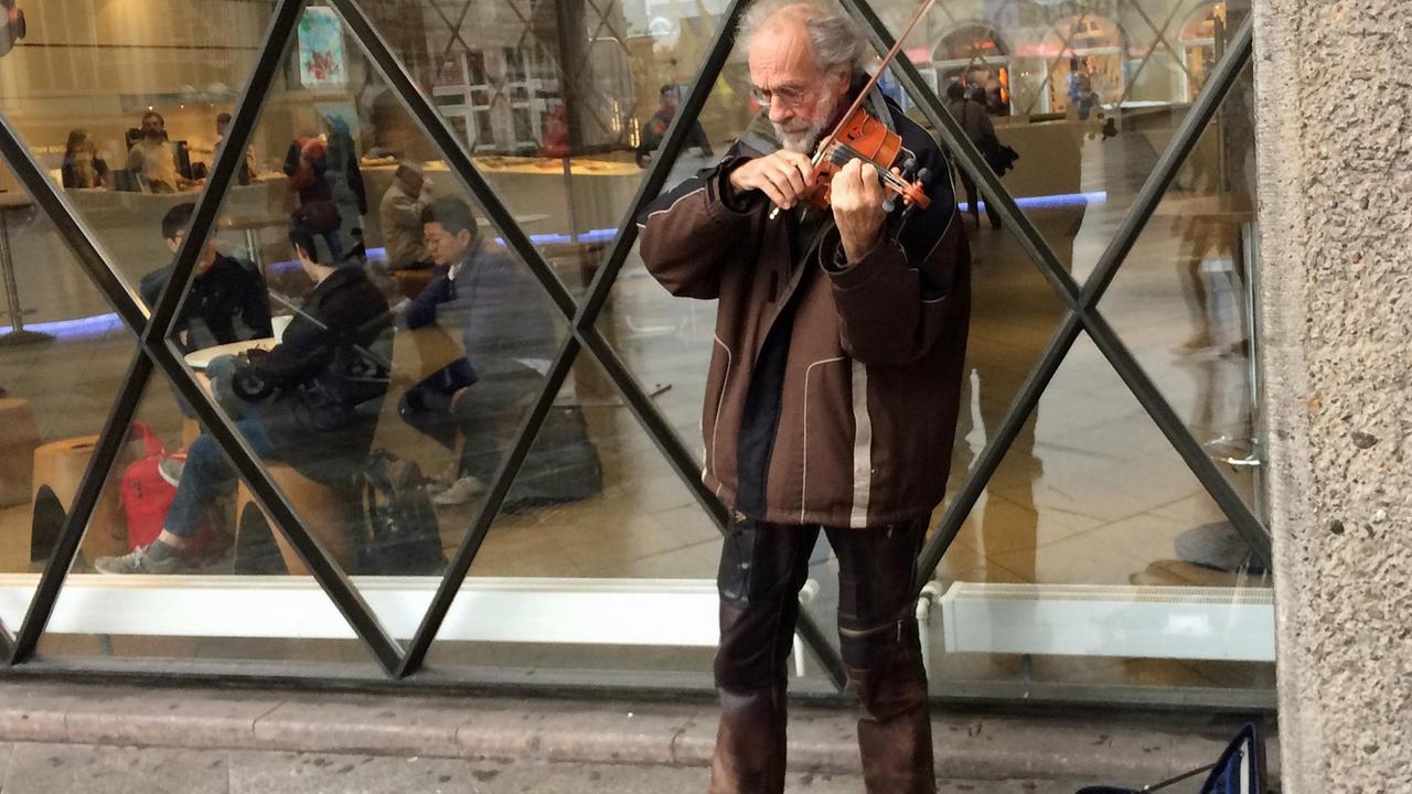 Der Straßenmusiker Klaus Wrochem spielt auf seiner Geige vor einem Schaufenster auf der Kölner Domplatte.