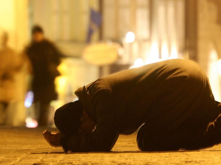 Ein Bettler sitzt bei Minusgraden in gebückter Haltung auf seinen Knien