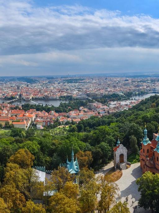 Blick über einen grünen Hügel zur Stadt Prag, die von der Moldau durchzogen wird.